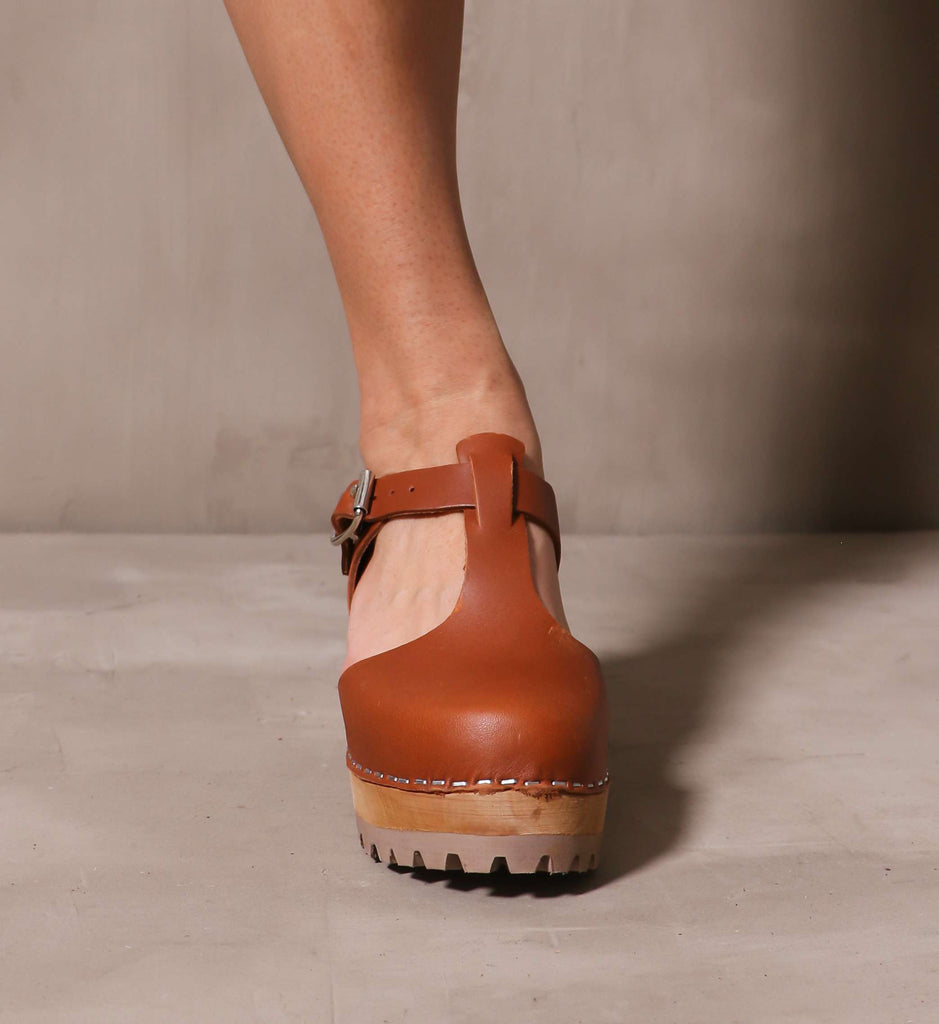 front of the round toe madeline t strap swedish leather clog on model standing on cement background