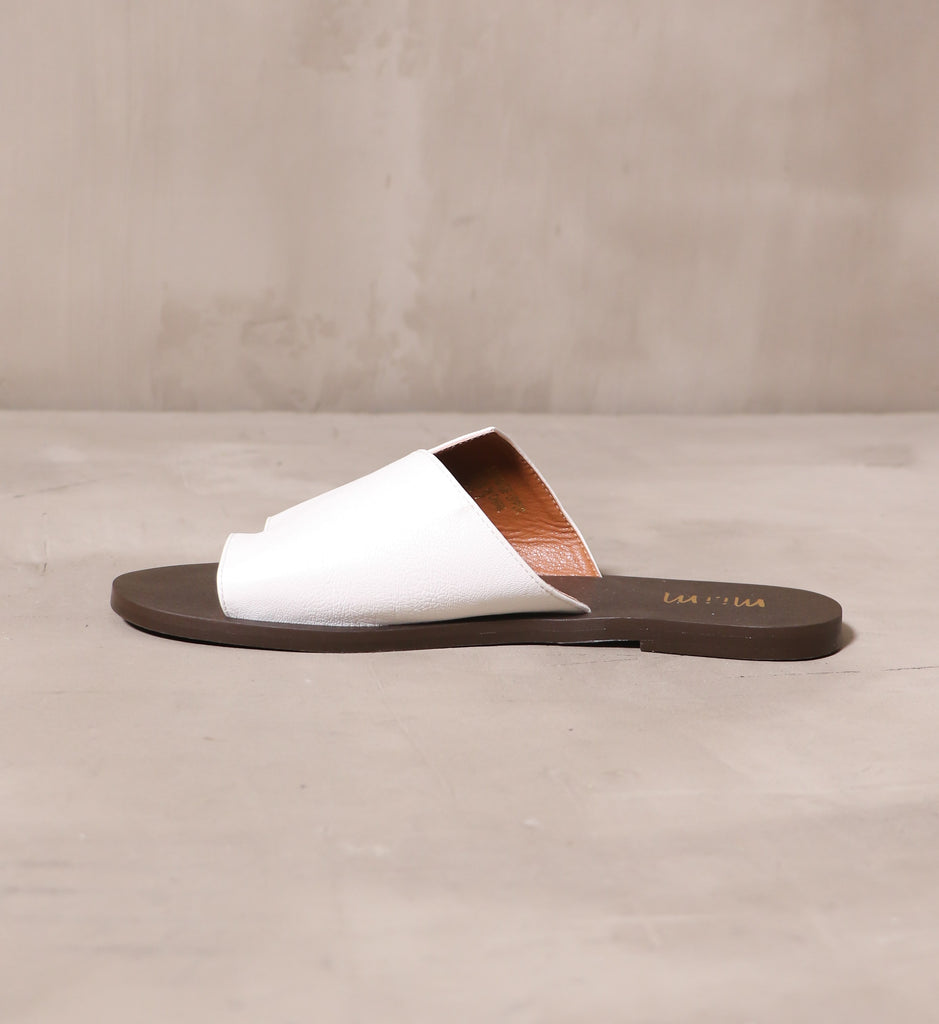 inner side of the white back toe you slide sandal with dark brown sole on cement background