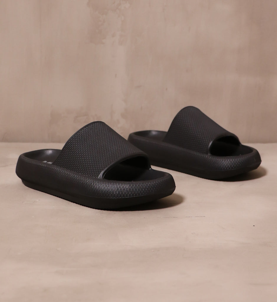 pair of black late to the foam party mia slip on slides angled on cement background