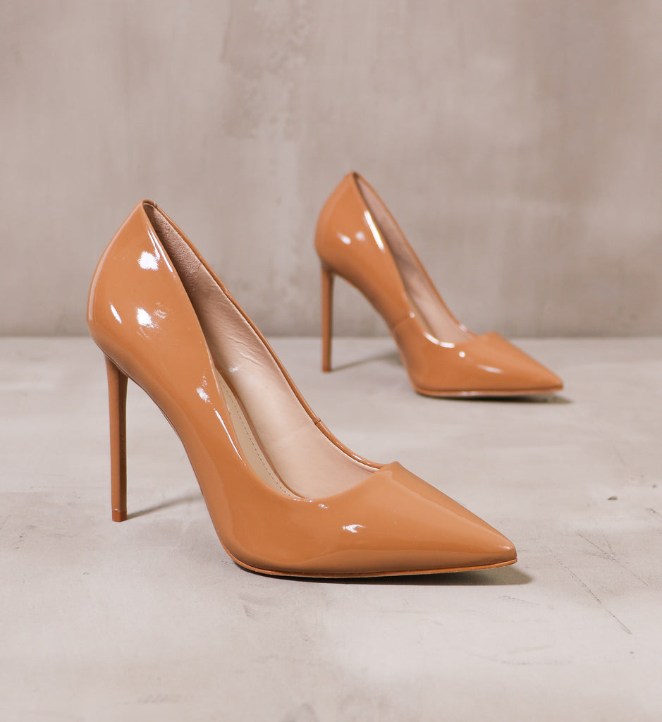 pair of tan patent leather double pump latte heels angled on cement background