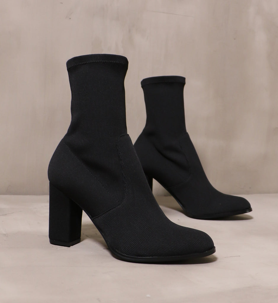 pair of all black knit happens boots angled on cement background