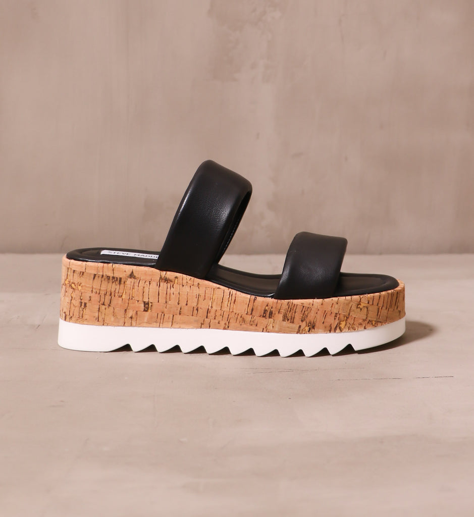 outer side of the black sole purpose platform sandal with chunky cork sole and white tread on cement background