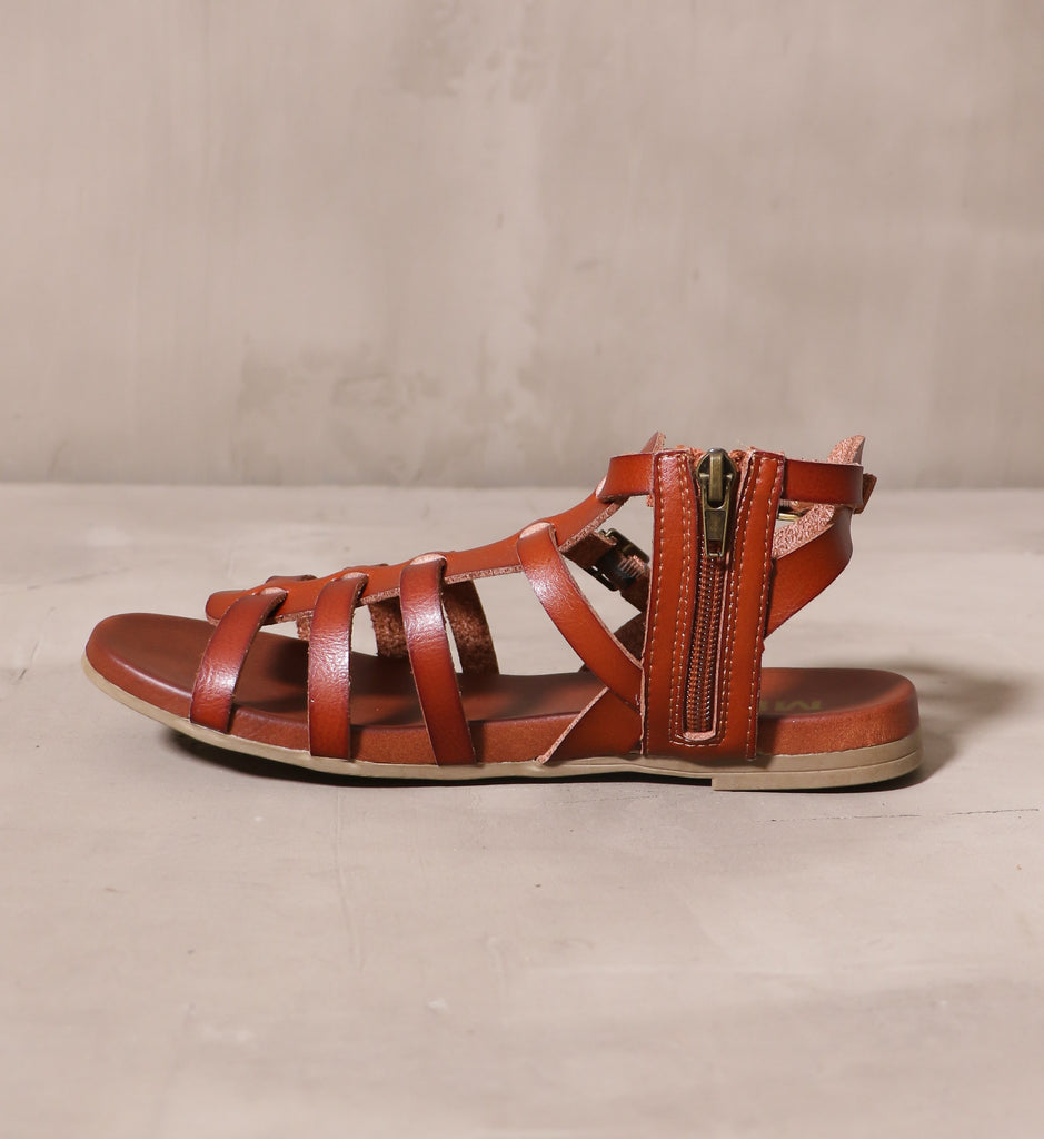 inner side showing the metal zipper pull on the cognac strappy makes me happy sandal on cement background