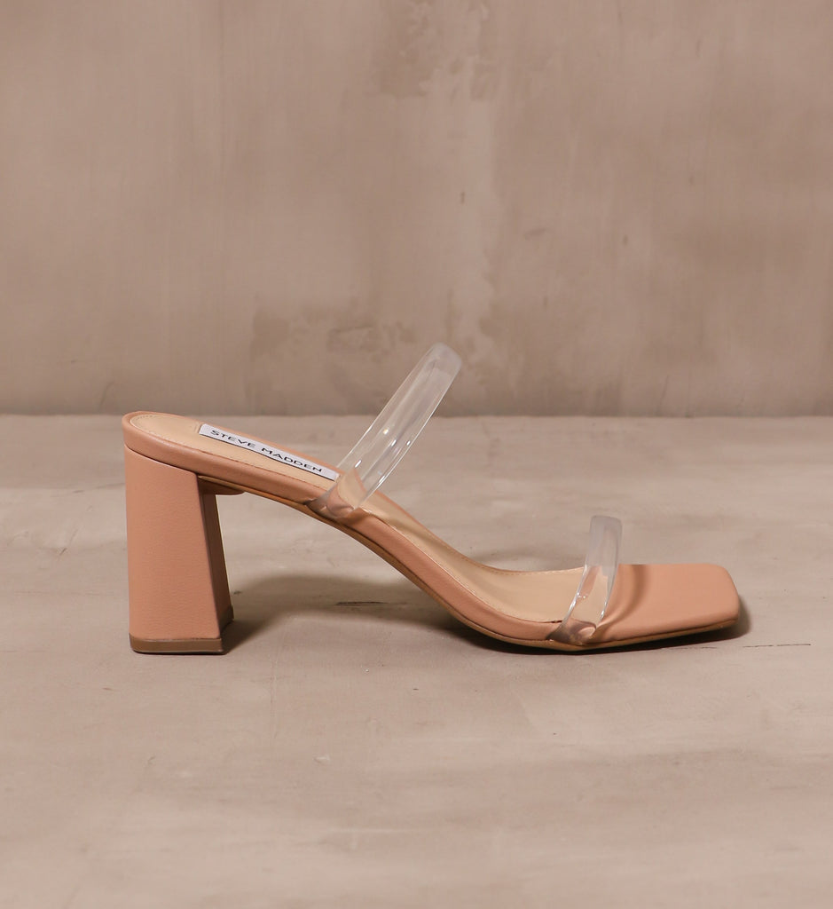 outer side of transparently timeless heel with slip on silhouette with two clear straps on a tan sole 