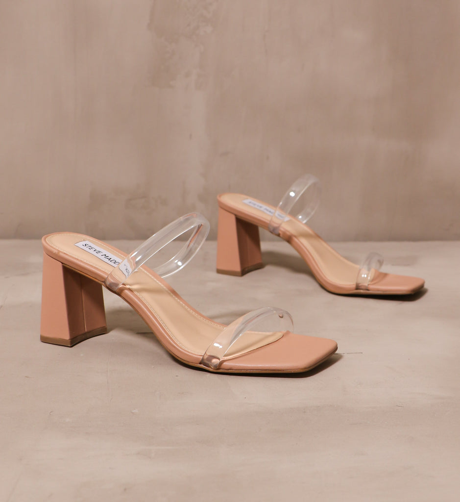 transparently timeless heel with thin clear rubber straps across the bridge and vamp with tan sole on cement background