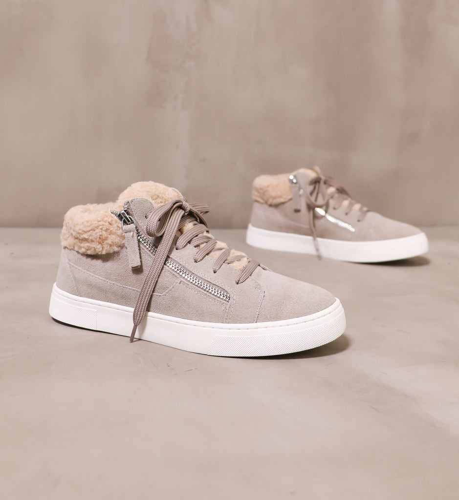 pair of warm feelings sneaker with taupe suede upper and beige faux fur trim on the warm feelings sneakers angled on cement background