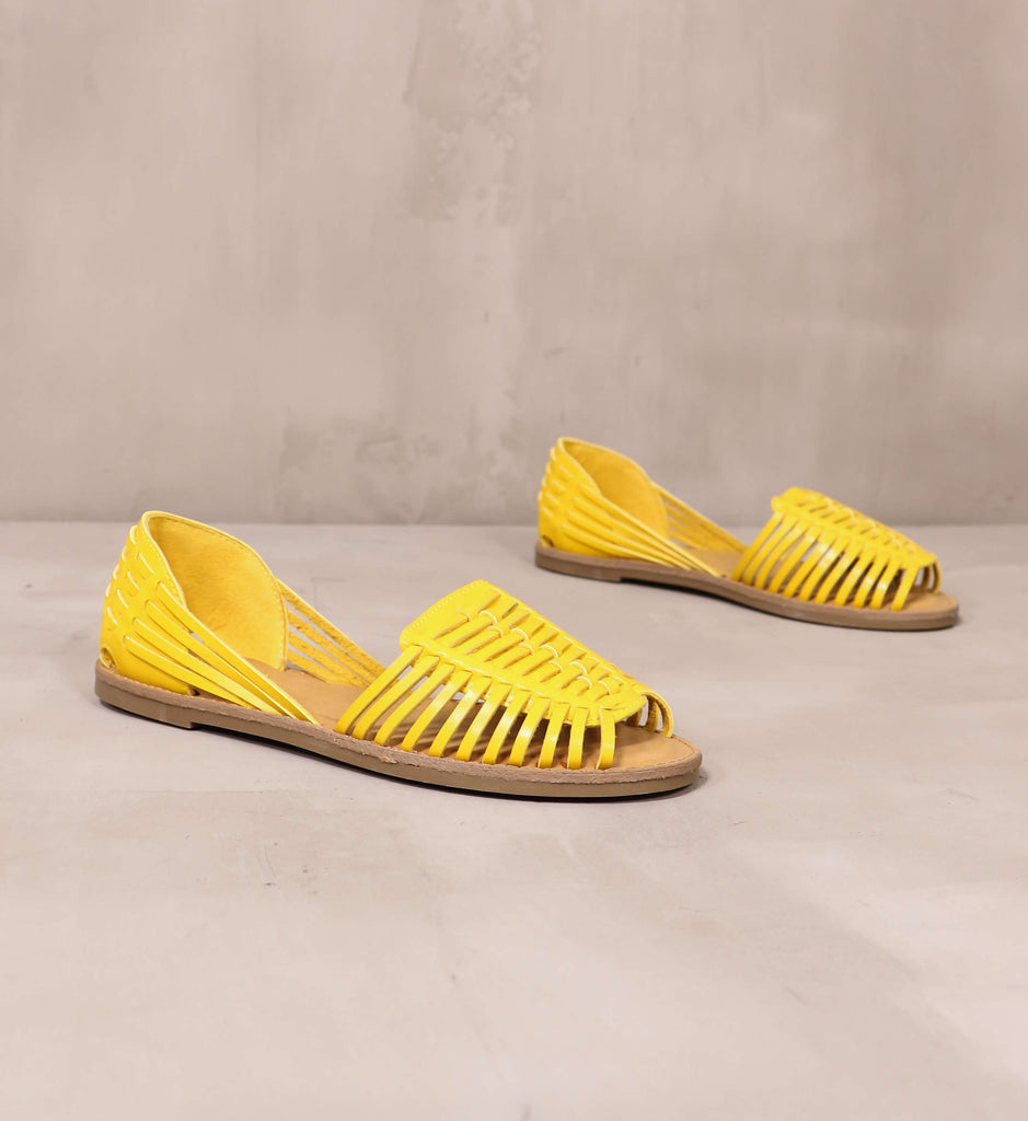 pair of yellow leather weave it to me sandals angled on cement background