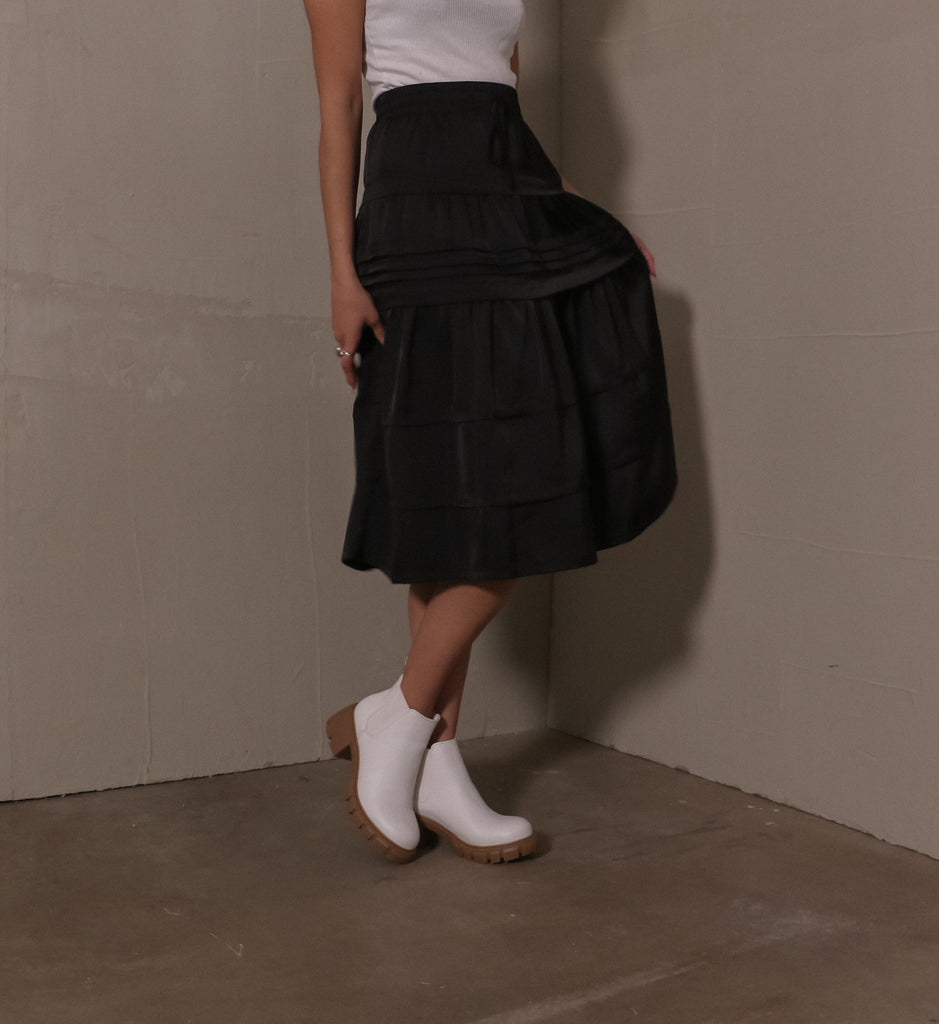model standing on cement floor wearing white tee, black skirt, and white lug sole in a quandry ankle boots
