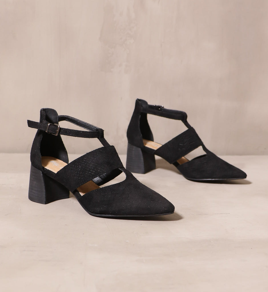 pair of black wine and dine heels with pointed toe silhouette and cutout details angled on cement background