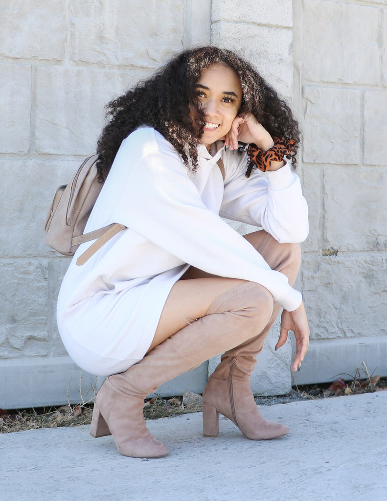 Model crouching in white hoodie dress and she's tall that taupe boots