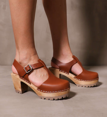 pair of model standing in the brown leather madeline t strap clogs on cement background