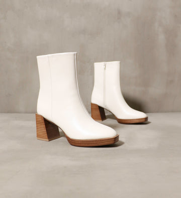 A pair of cream booties with stacked wood platform on a cement background - Elle Bleu