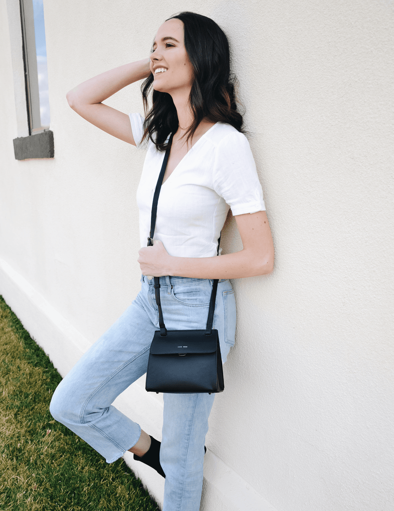 Model standing outside in tee, denim, black knit happens booties and christy crossbody