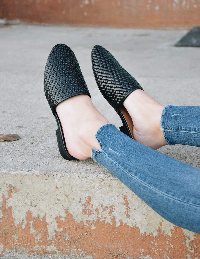 Girl putting feet up on concrete steps wearing black lolli flats and denim
