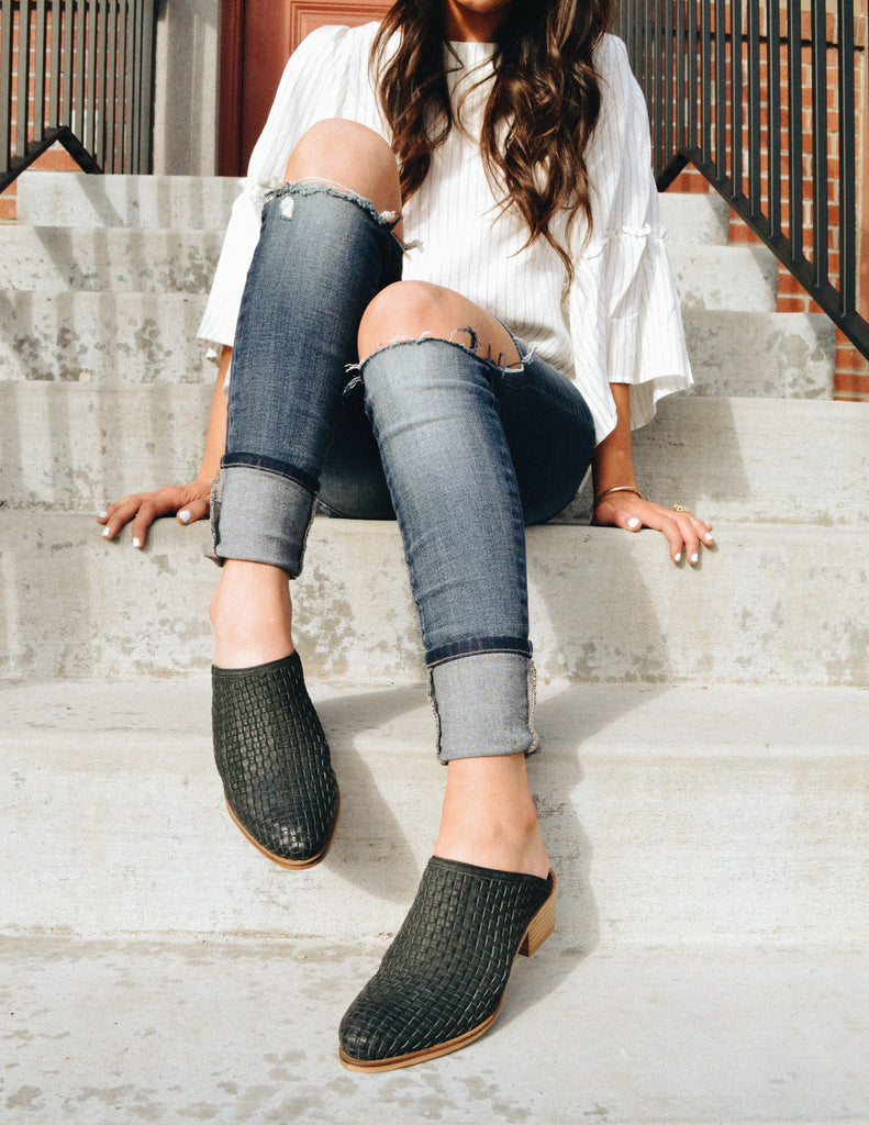 Girl sitting on steps in denim, white top, and black mules 