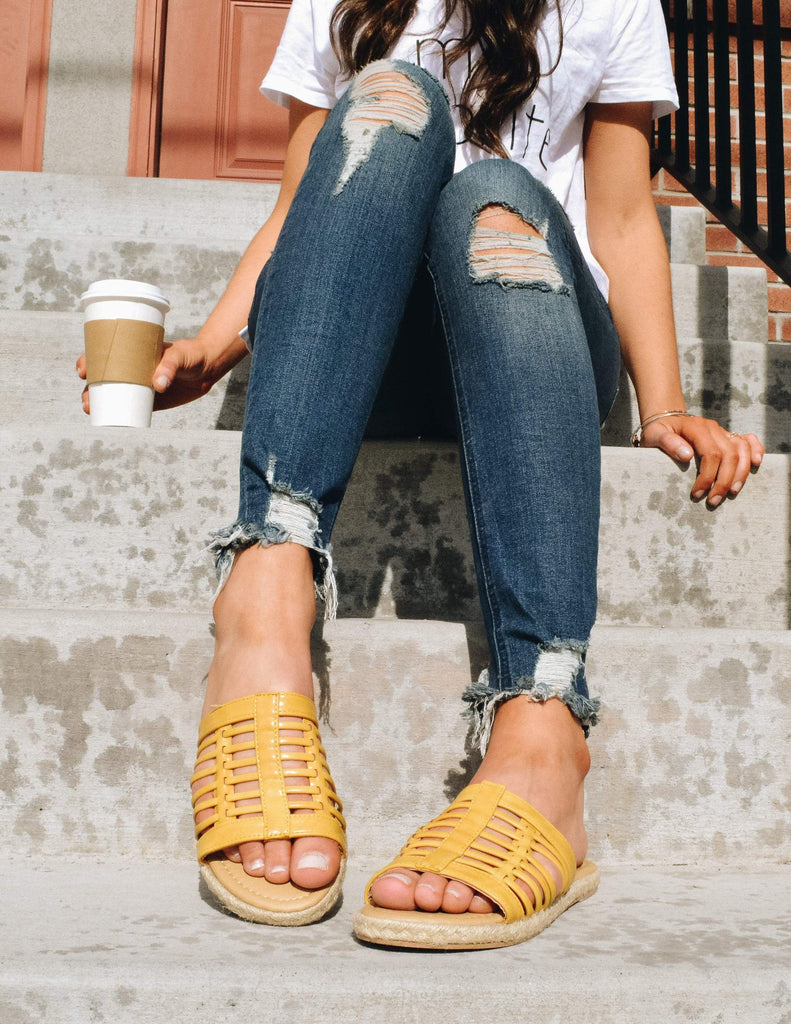 Model sitting on steps outside in tee, denim, and yellow sandals