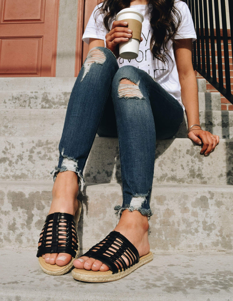 Model sitting on concrete steps wearing tee, denim, and black sandals