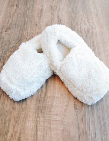 Creme faux fur warmies slippers on wood background - elle bleu