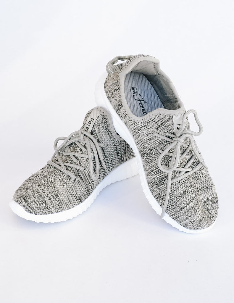 Grey woven sneakers stacked on heel on another on white background