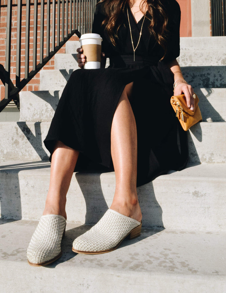 Girl sitting on steps holding coffee & clutch in black dress and mules