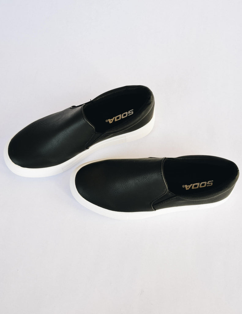 Black slip on sneakers laying flat on white background - elle bleu shoes