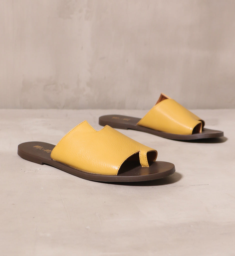 back toe you mustard vegan pebble leather asymmetrical slide sandals angled on cement background