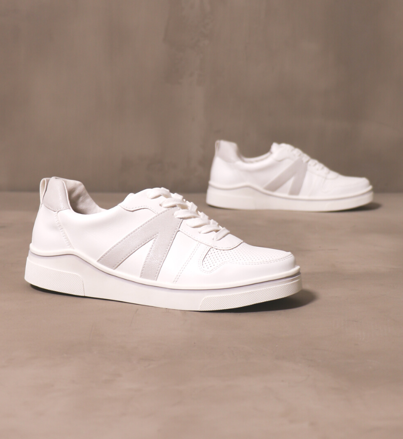 pair of between the lines sneakers in off white set on a cement background.