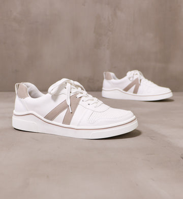 pair of white taupe between the lines sneakers angled on cement background