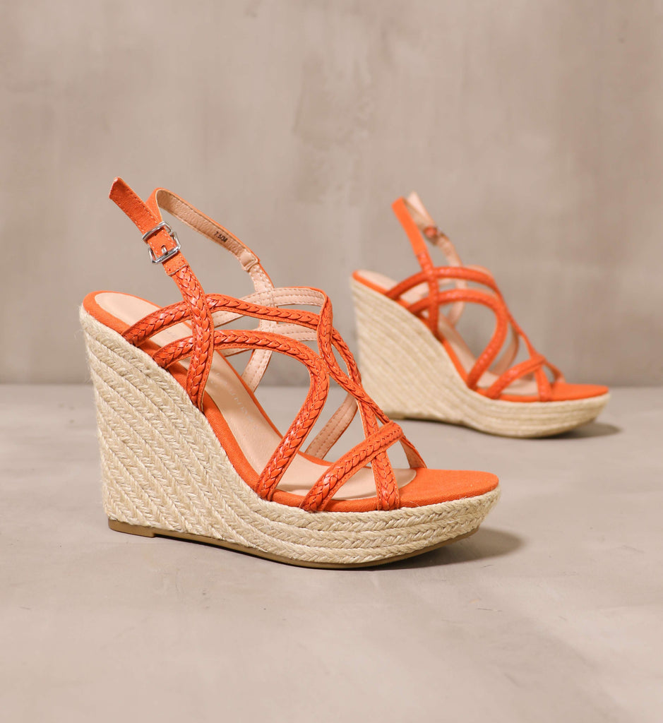 pair of orange braid for walking wedge with raffia soles angled on cement background
