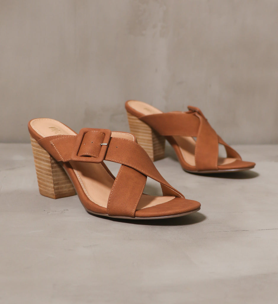 pair of brown buckle or nothing heels with criss cross straps on a tan sole on cement background