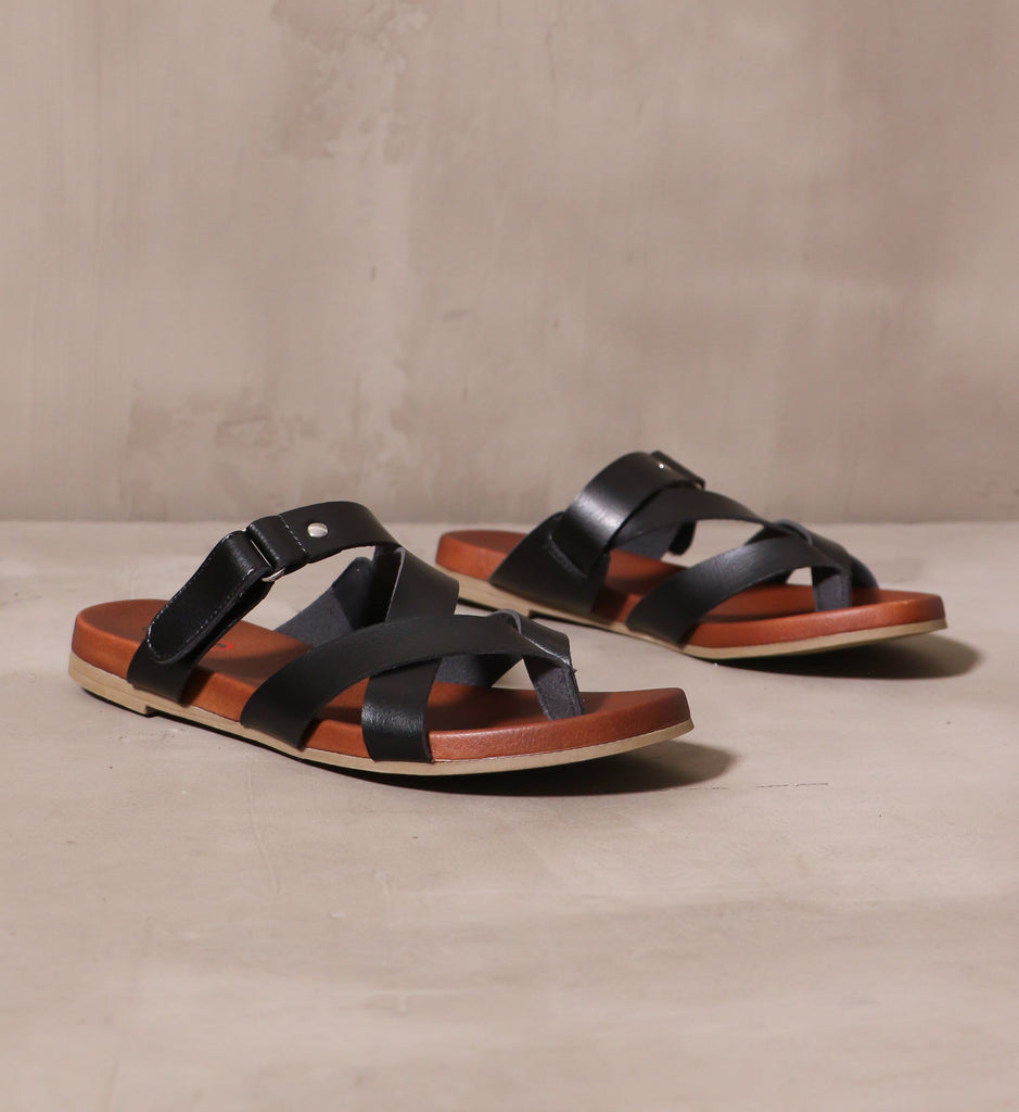 pair of black casually crossed sandals angled on cement background