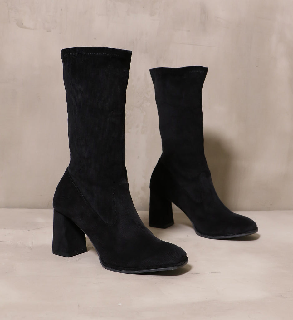 pair of all black cord ordered mid calf boots with block heels andlged on cement background