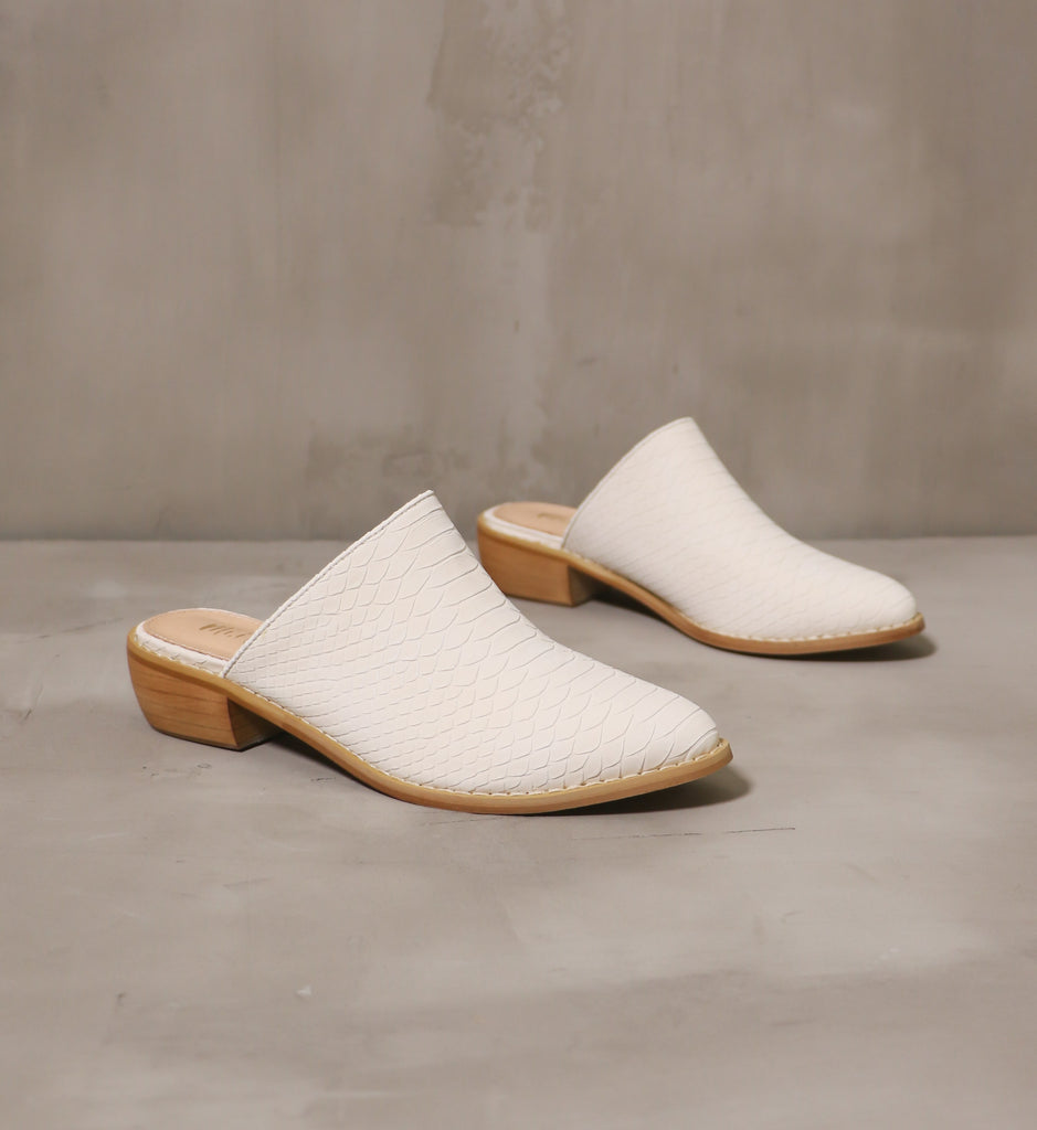 pair of cream of the croc textured mules with wood soles on cement background