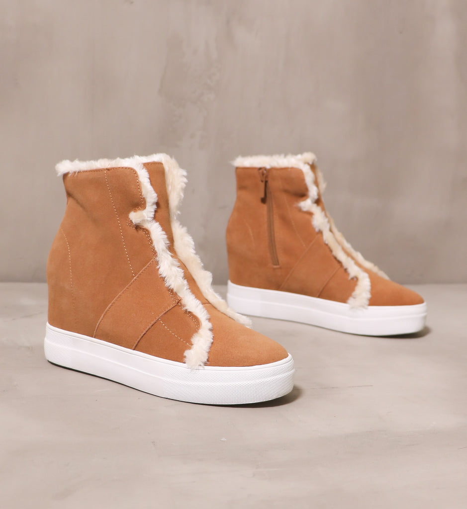 pair of tan fur wedge and fur all wedges with white rubber soles on cement background
