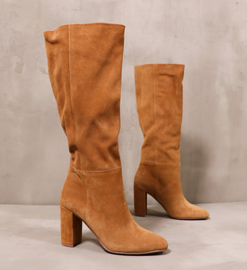 pair of honey brown suede leather tall boots angled on cement background