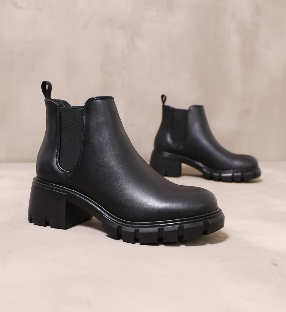 pair of all black in a quandry boots angled on cement background
