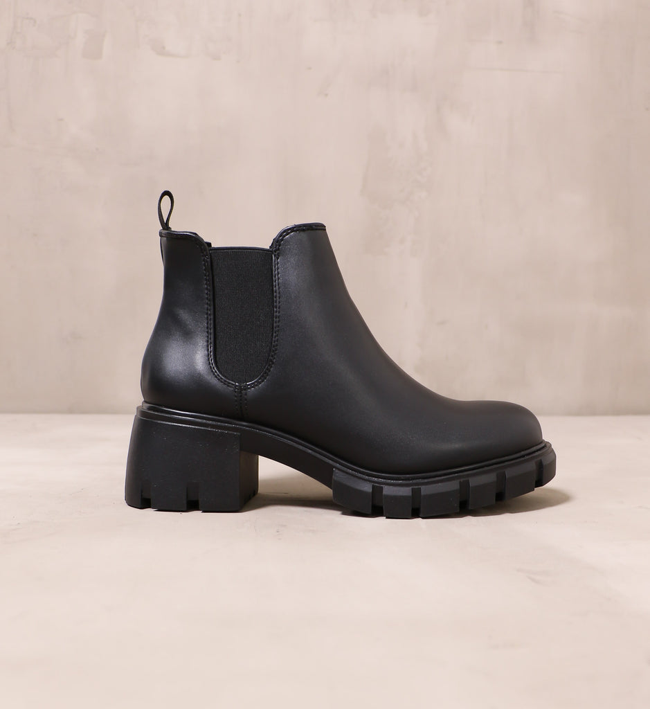 outer side of the all black in a quandry boot with chunky rubber sole and black elastic panel near ankle