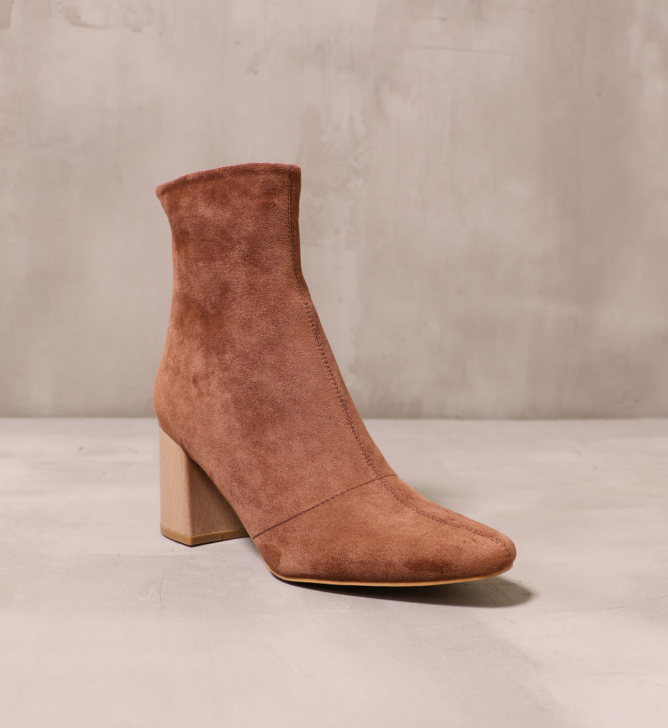 front of the almond toe chestnut brown suede booties with block heel on cement background