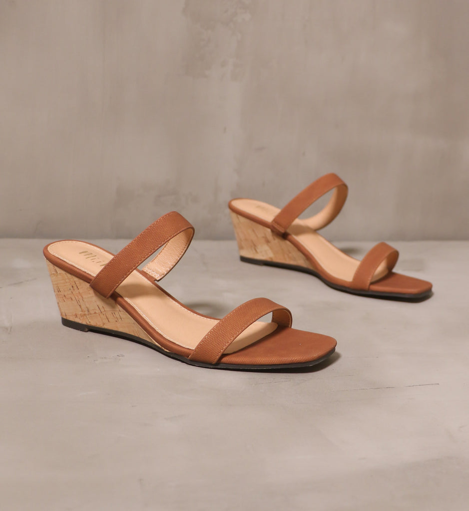 pair of kim and cork take new york brown wedge sandals angled on cement background