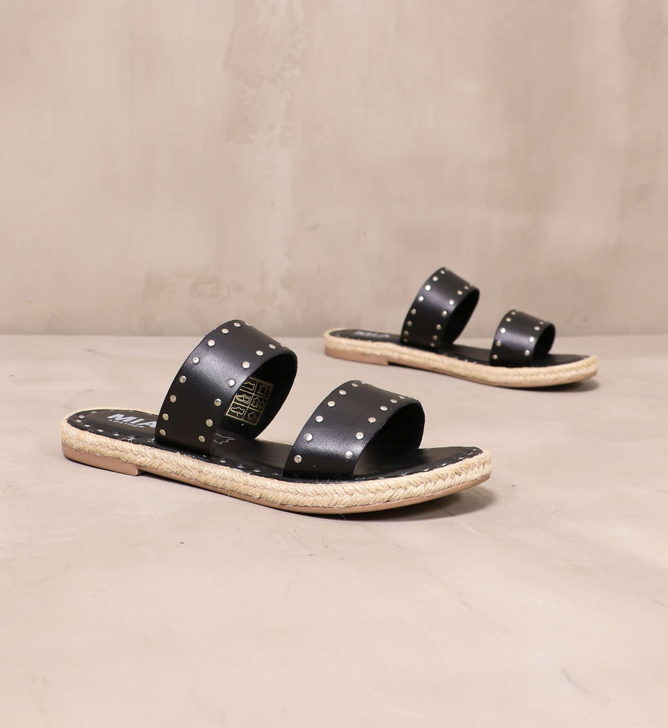 pair of black leather let the stud times roll sandals angled on cement background