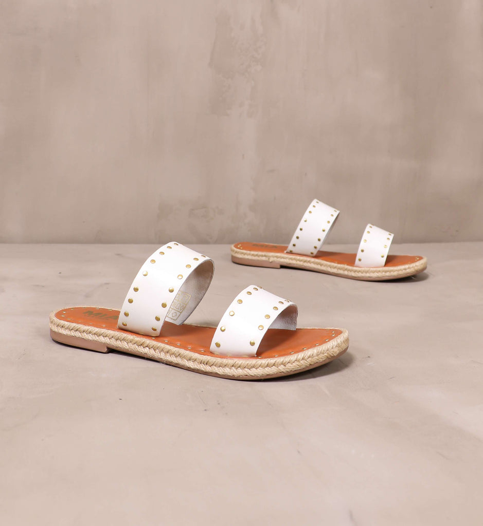pair of white strap let the stud times roll sandals angled on cement background