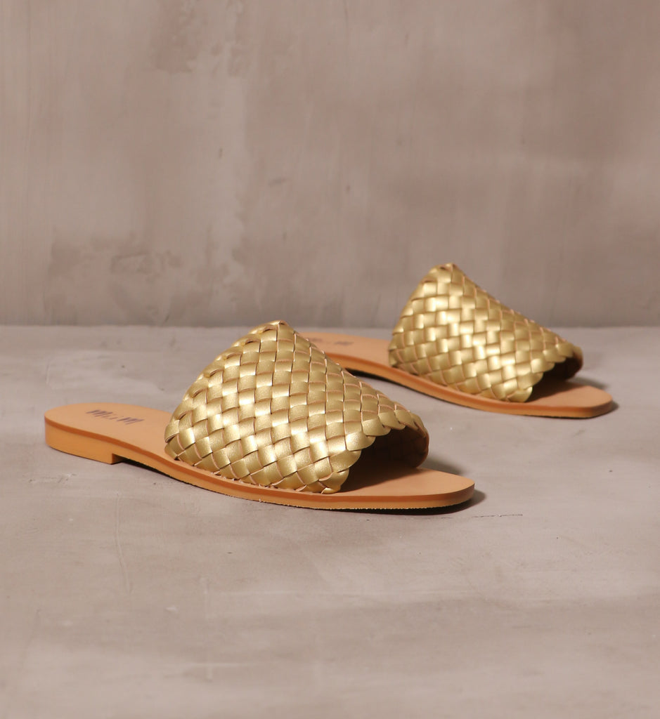 gold leather straps woven into a thick strap attached to tan sole on a pair of the woven one slides