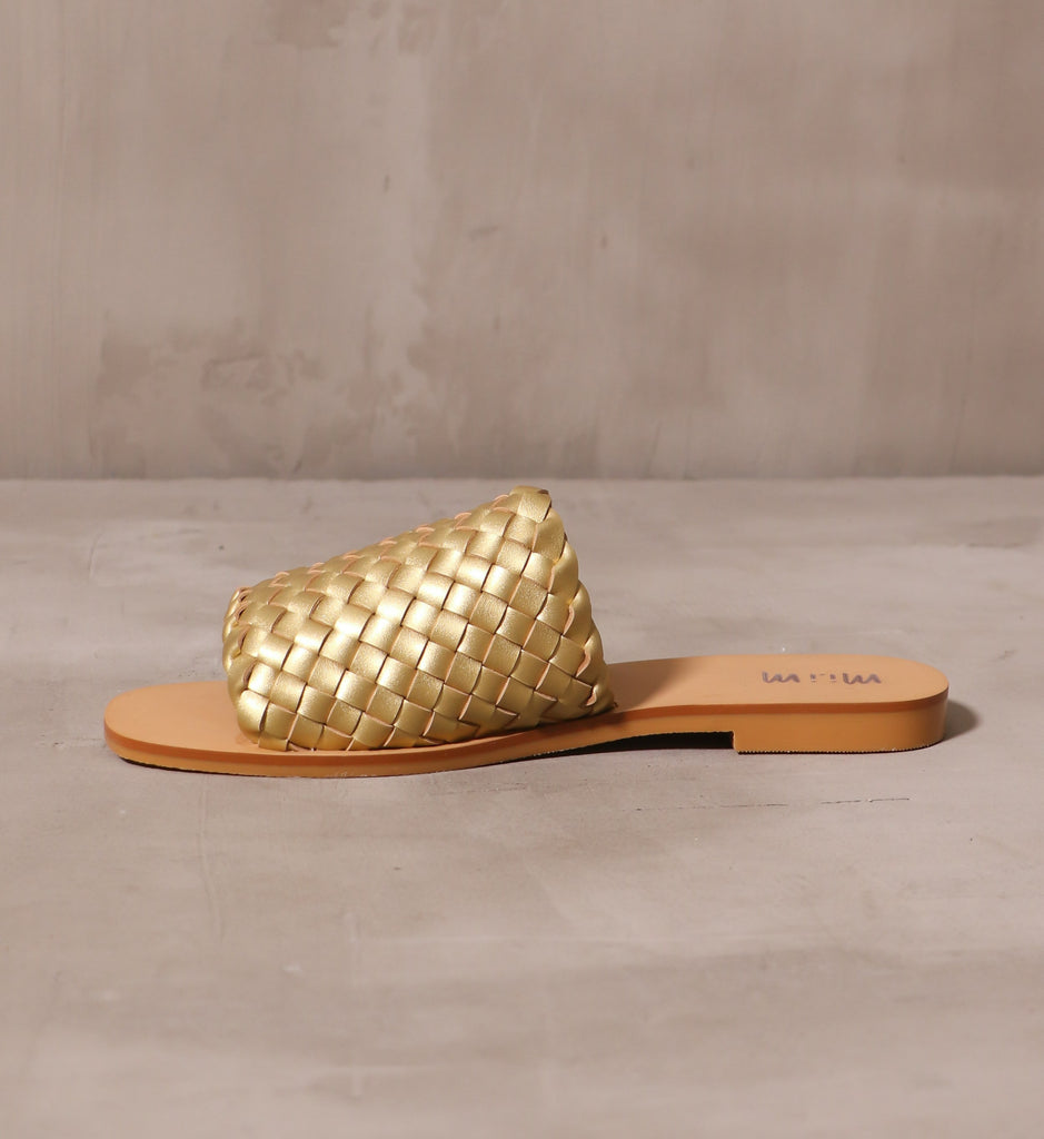 inner side of the gold woven one slide sandal attached to tan sole on cement background