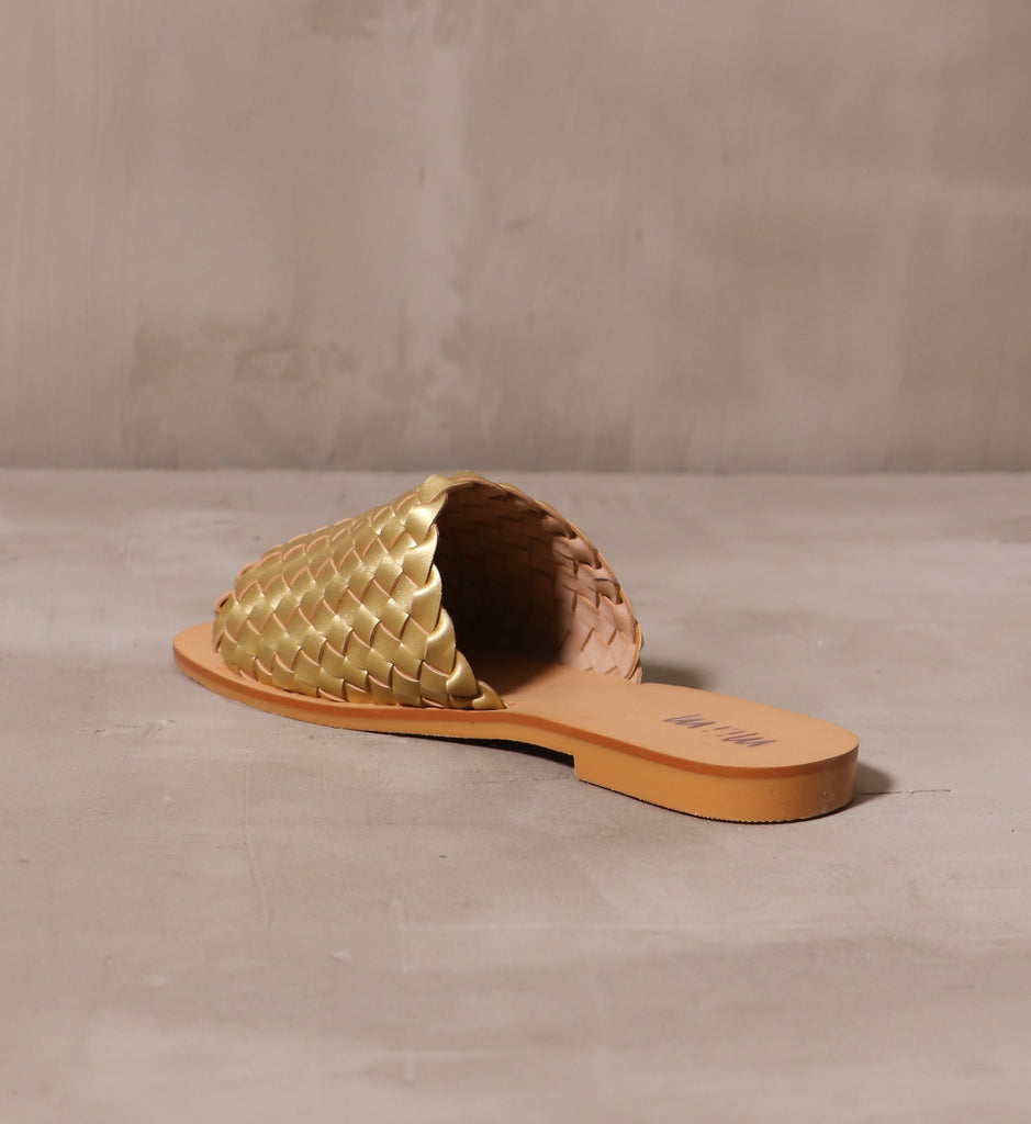 back of the open back woven one slide sandal with tan lining on the gold woven strap