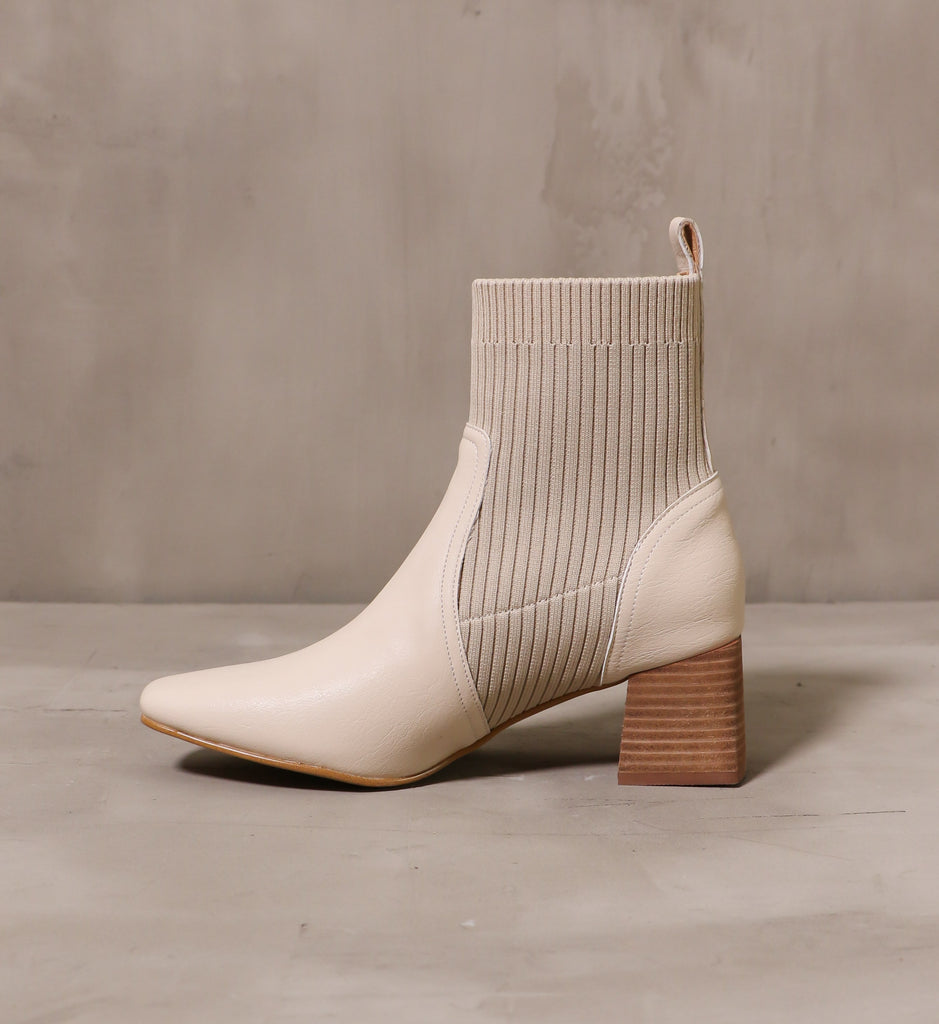 inner side of the beige my sweater half ankle boot with stacked block wood heel on cement background