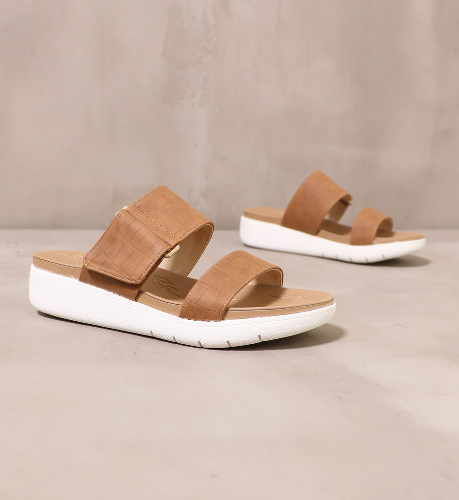 pair of tan leather strap on, two strap sandals angled on cement background