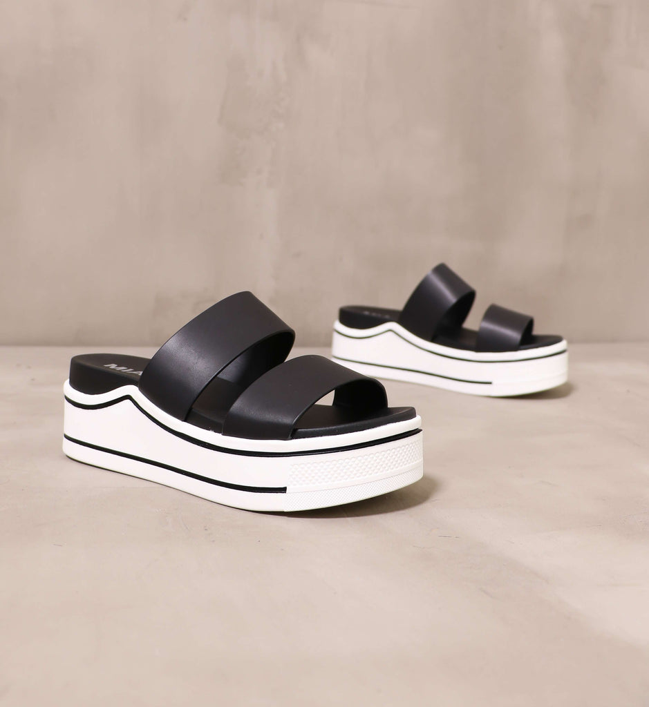 pair of black upper and white chunky sole platform an opinion sandals angled on cement background