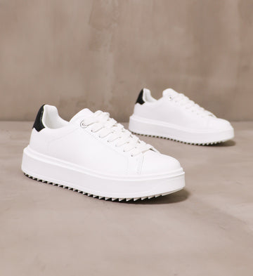 pair of all white play the field sneakers angled on cement background