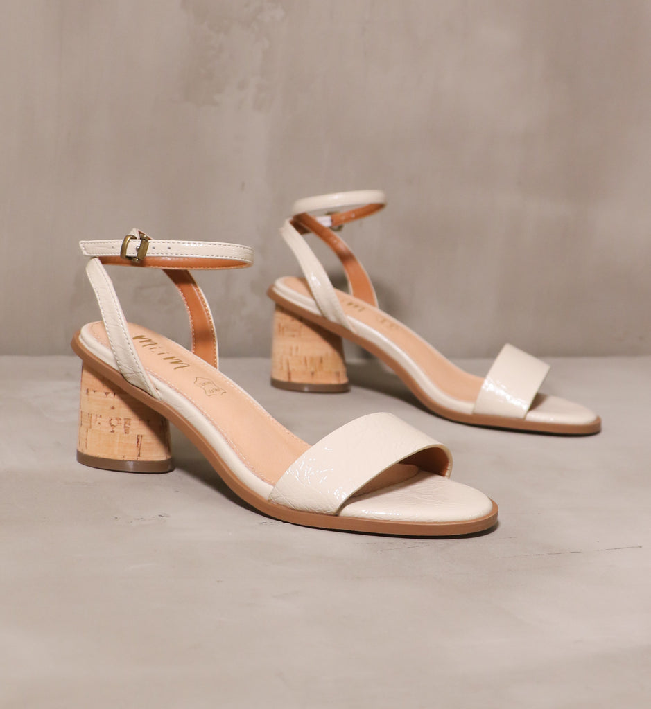 pair of beige thin straps on the pop the cork heels angled on cement background