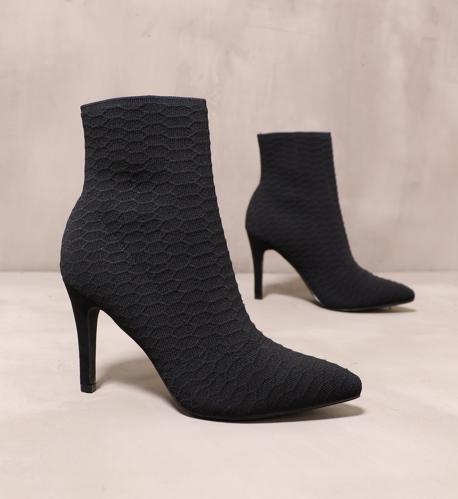 pair of all black textured sock it to me booties angled on cement background